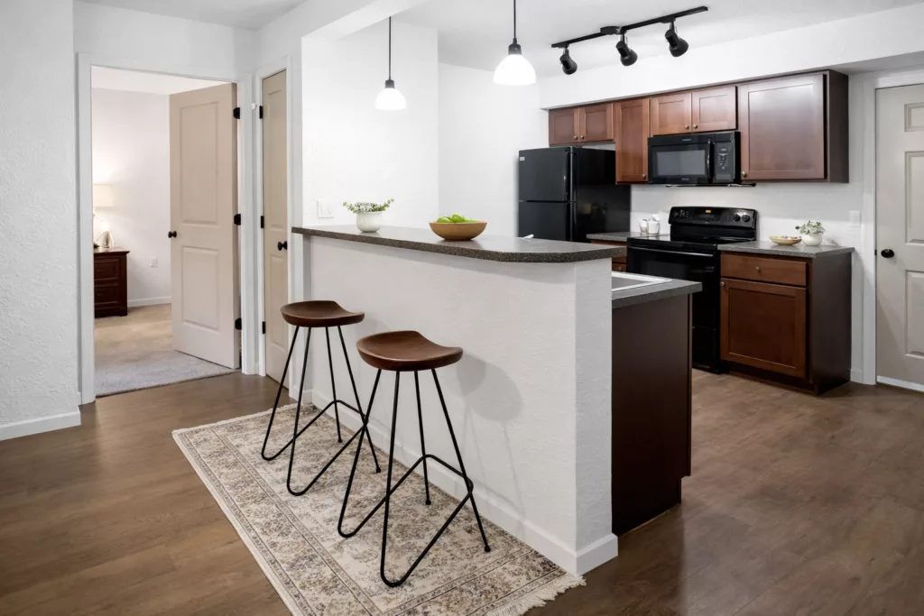 Modern kitchen with a white countertop, two bar stools, dark cabinets, black appliances, and track lighting.