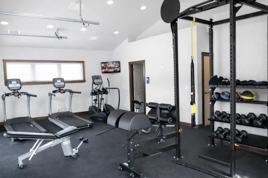 A well-equipped home gym with treadmills, weight machines, a rack of dumbbells, and an exercise bench.
