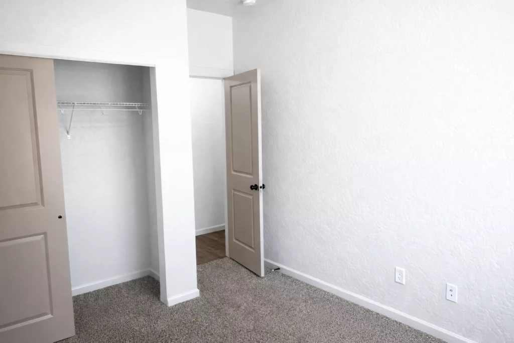 Empty room with textured white walls, an open closet, and a door slightly ajar.