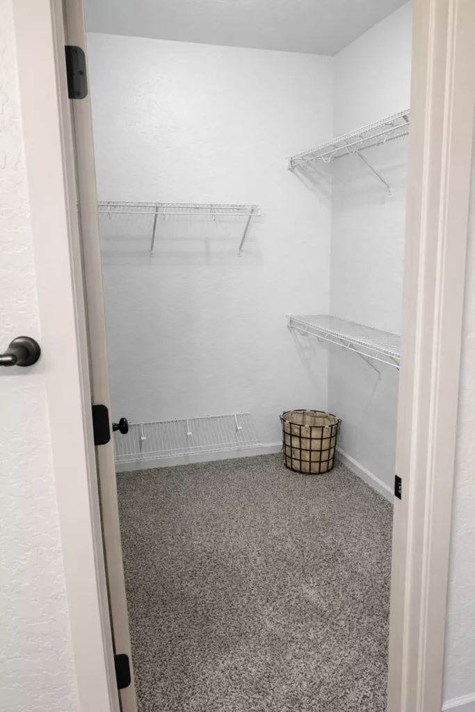 Empty walk-in closet with three wire shelves and a round laundry basket on a carpeted floor.