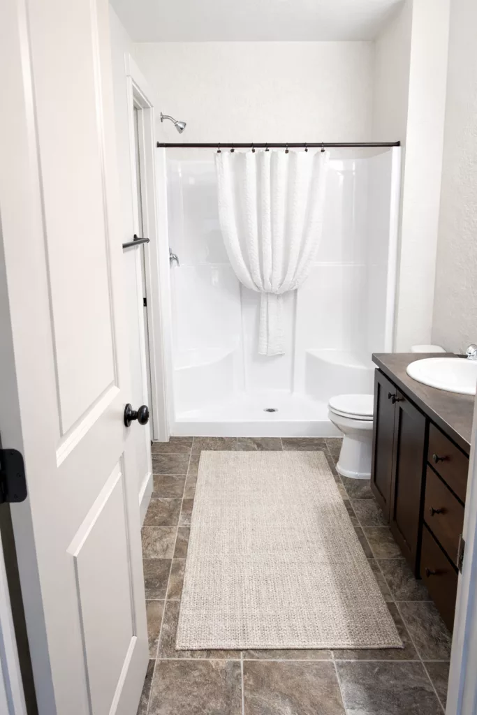 A small bathroom with a shower, curtain, vanity with mirror, and toilet on a tiled floor.