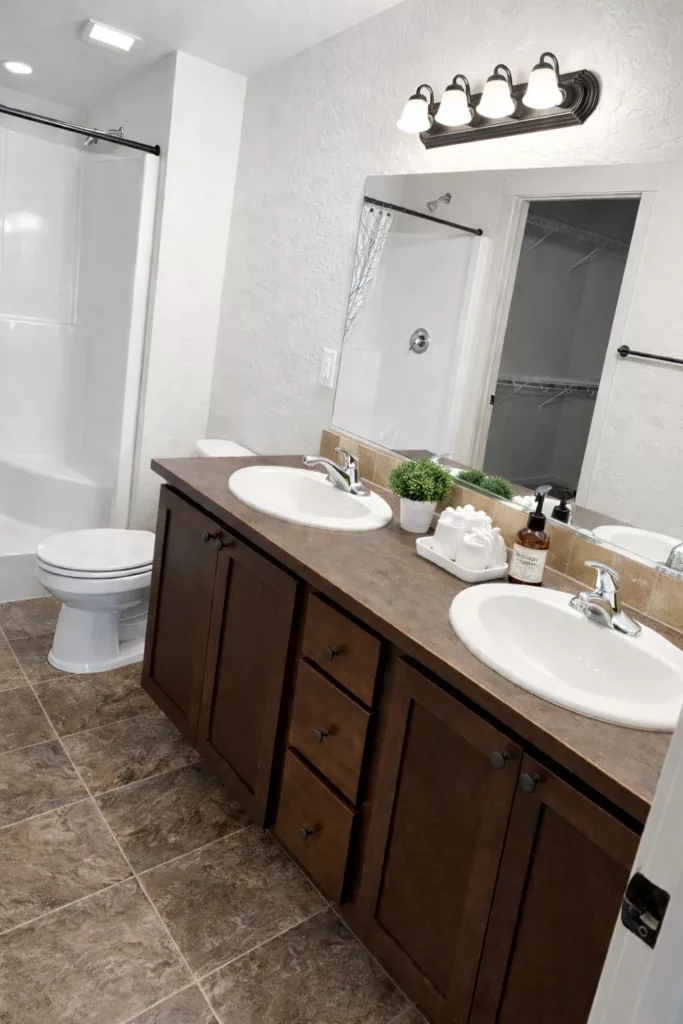 Double-sink bathroom with dark wood vanity, toiletries, and a large mirror above, adjacent to a bathtub with a curtain.