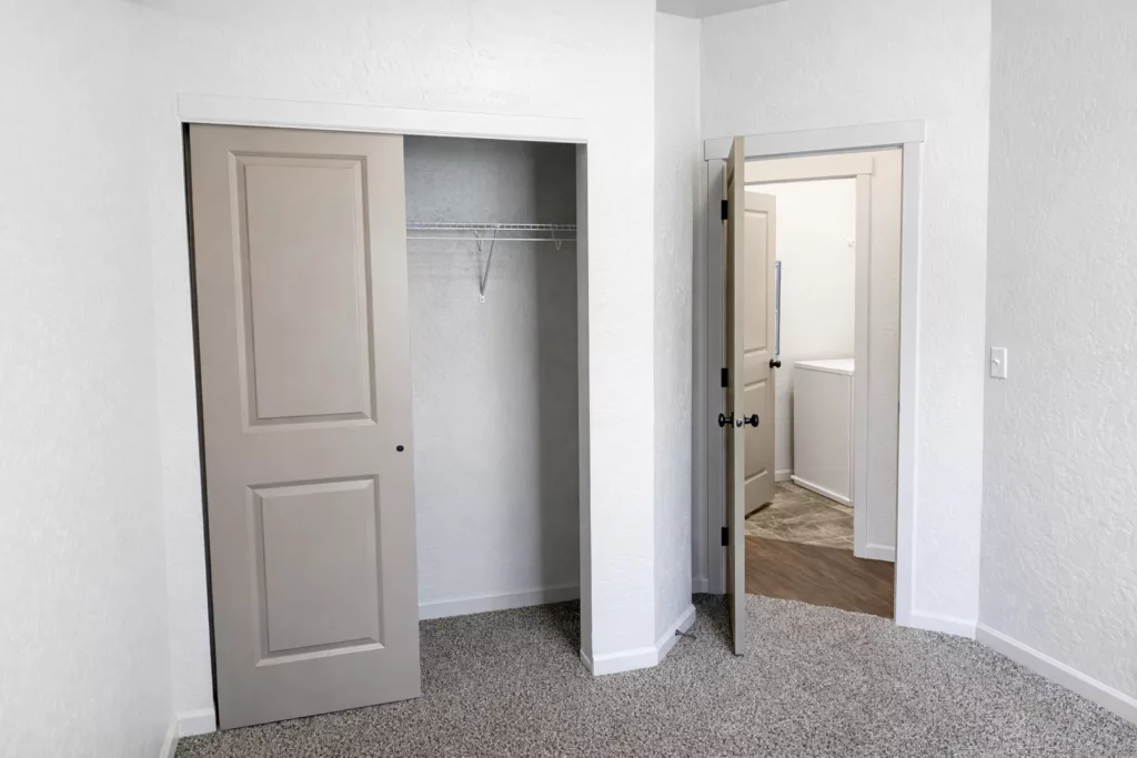 Empty room with a carpeted floor, an open closet with sliding doors, and an open door leading to another room.