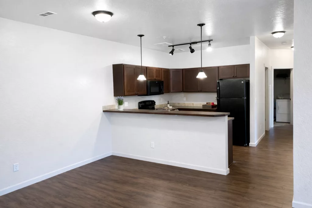 A modern kitchen with dark wood cabinets, black appliances, and a small island with pendant lighting in an open-plan space.