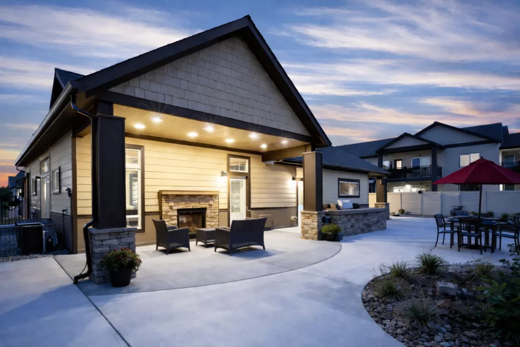 A modern single-story house with a spacious patio, outdoor furniture, and a well-lit facade against a dusk sky.