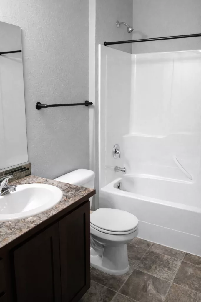 A modern bathroom featuring a white bathtub and shower, a toilet, a sink with a marble countertop, and a large mirror.