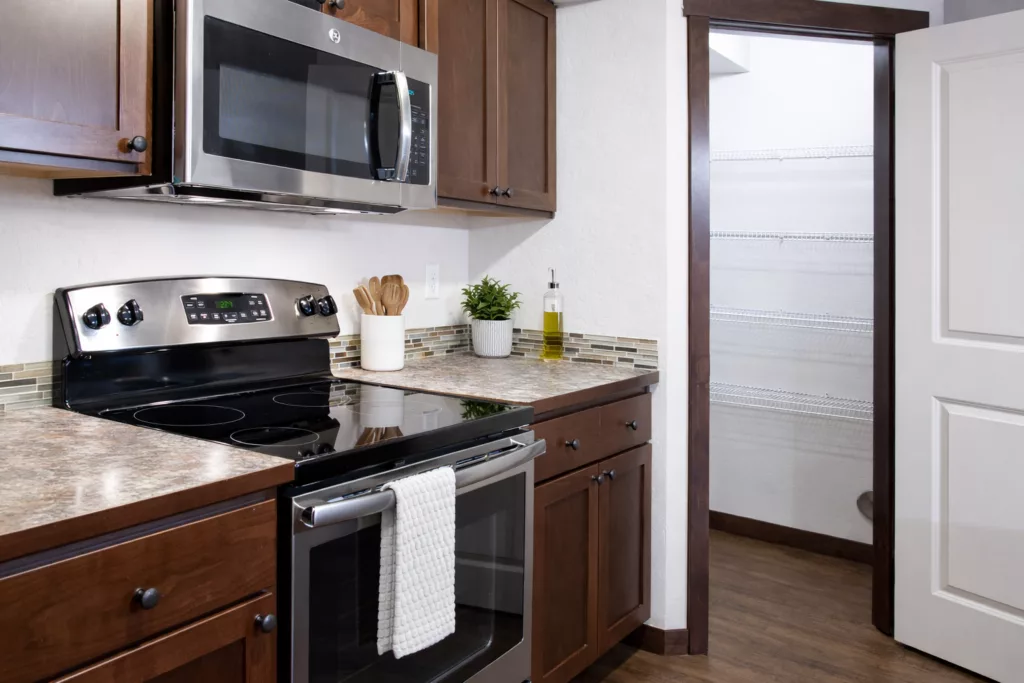 A modern kitchen with dark wood cabinets, stainless steel appliances, and an open pantry door.