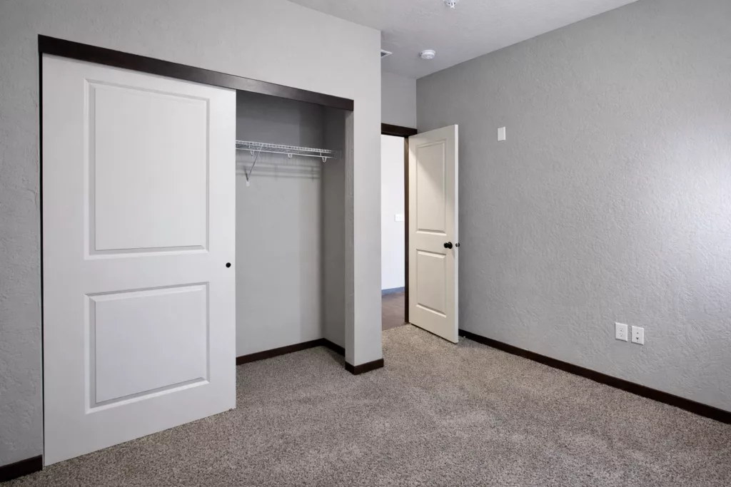 Empty room with gray walls, carpeted floor, an open sliding door closet, and a closed white door.