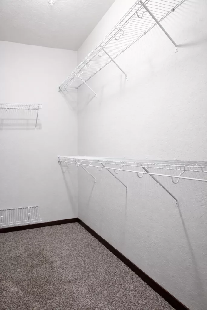 Empty walk-in closet with white wire shelving on the walls and carpeted floor.