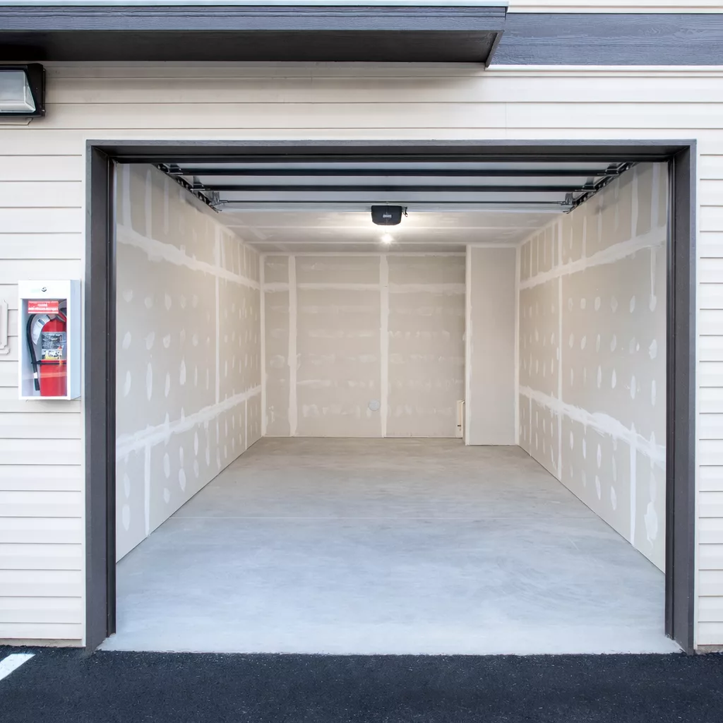 Empty single-car garage with drywall interior and a fire extinguisher mounted on the exterior wall.