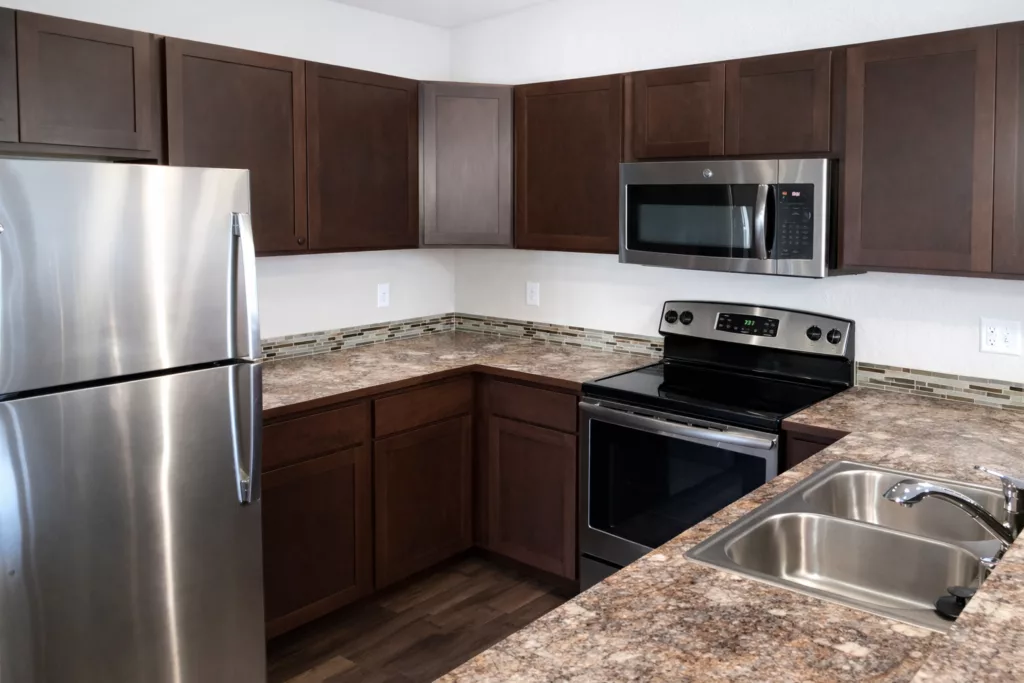 A modern kitchen with stainless steel appliances, brown cabinets, and a granite countertop.