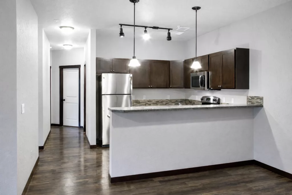 A modern kitchen with dark wood cabinets, stainless steel appliances, and a stone-tiled backsplash.