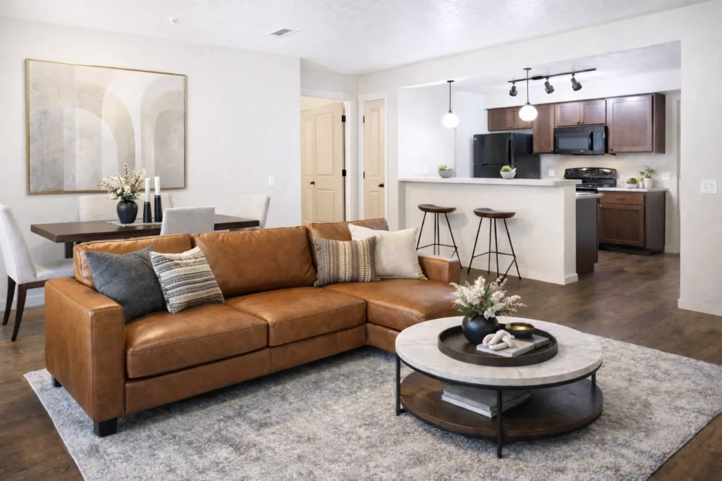 Spacious living room with a brown leather sofa, patterned cushions, round coffee table, and an open kitchen in the background.